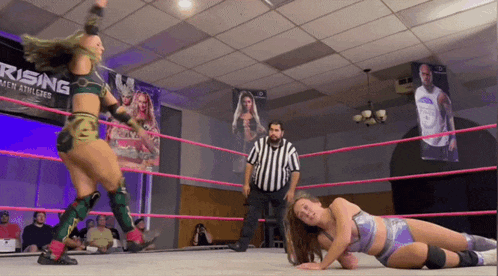 two women wrestle in a ring with a sign that says rising in the background