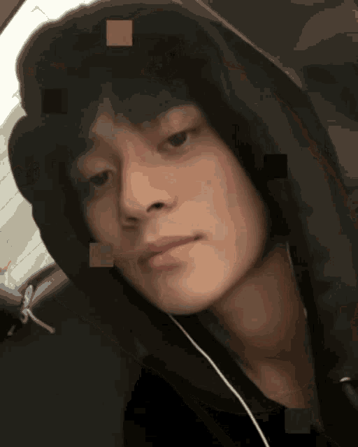 a young man wearing a black hoodie and earphones looks at the camera