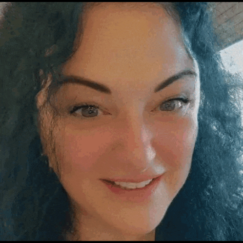 a close up of a woman 's face with curly hair and blue eyes smiling .