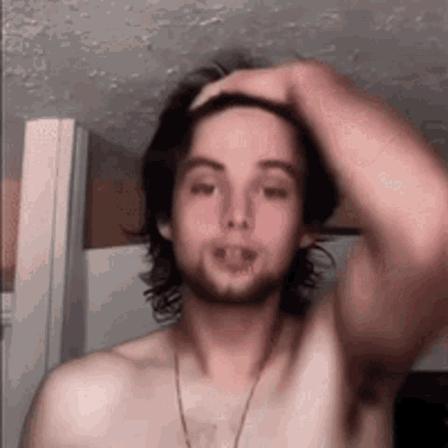 a shirtless man with a beard is holding his head while wearing a necklace .