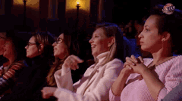 a group of women are sitting in a theatre laughing and clapping their hands .