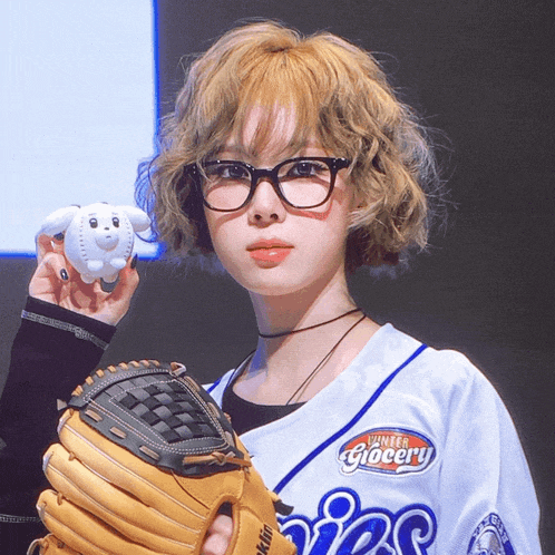a girl wearing a number grocery jersey holds a baseball and a glove