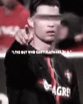 a man wearing a hat and a black shirt with the word agree on it is pointing at the camera .