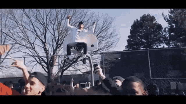 a man is sitting on top of a basketball hoop with his arms in the air