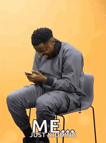a man is sitting in a chair looking at his phone with the words me just kidding behind him
