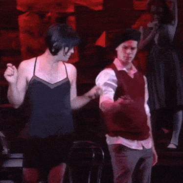 a man in a red vest is holding the hand of another man in a black dress .