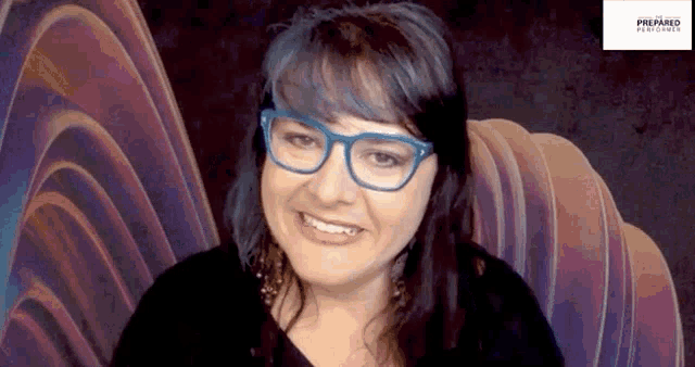 a woman with blue hair and glasses is smiling in front of a purple background .