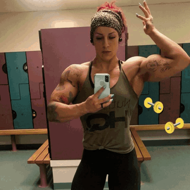 a woman taking a picture of herself in a locker room with dumbbells in the background