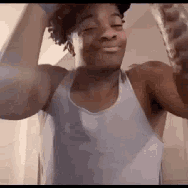 a young man in a white tank top is flexing his muscles and smiling .