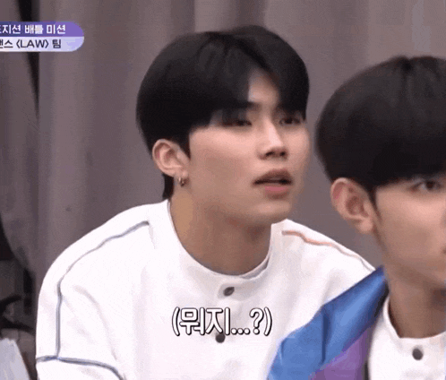 two young men are sitting next to each other and one of them is wearing a white shirt and earrings .