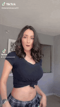 a woman in a black crop top and plaid skirt is dancing on tiktok .