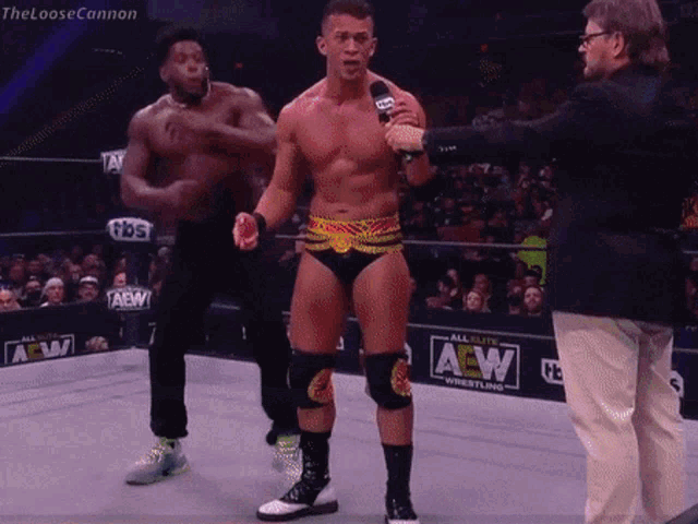 a wrestler is talking into a microphone in front of a aew sign