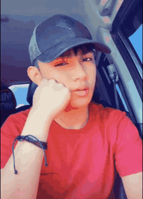 a young man wearing a hat and a red shirt is sitting in the back seat of a car