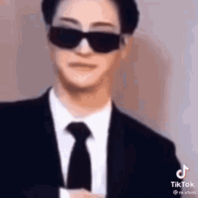 a man in a suit and tie is wearing sunglasses and making a funny face .