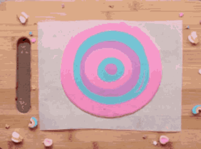 a person is painting a pink and blue swirl on a piece of wax paper with a brush .