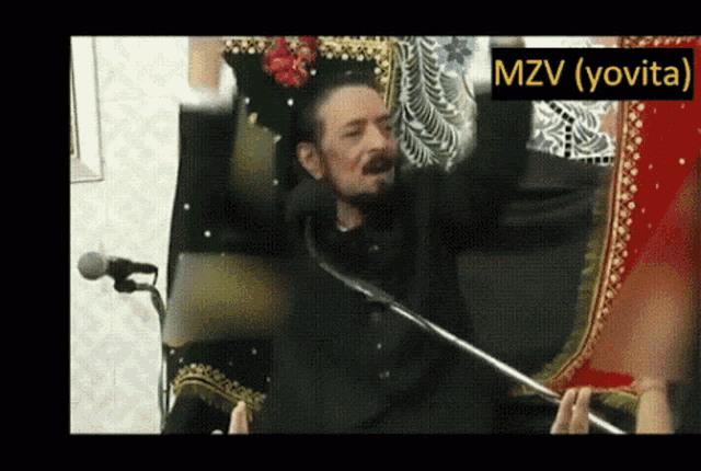 a man with a beard is sitting in front of a microphone with the words mzv ( yovit ) above him