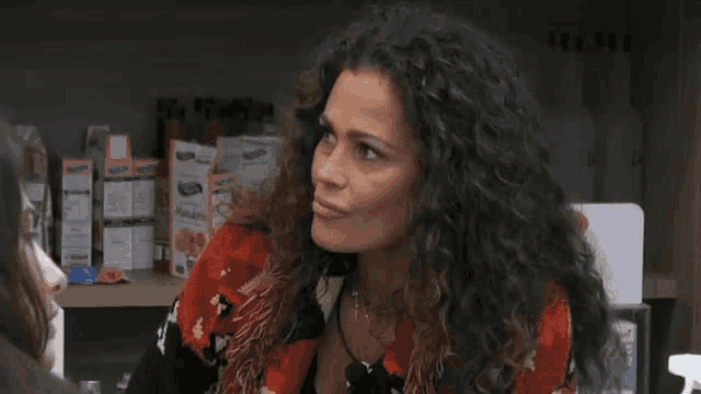 a woman with curly hair is sitting in front of a shelf with boxes of food on it .