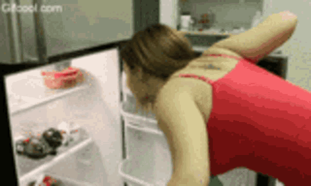 a woman in a red tank top opens a refrigerator