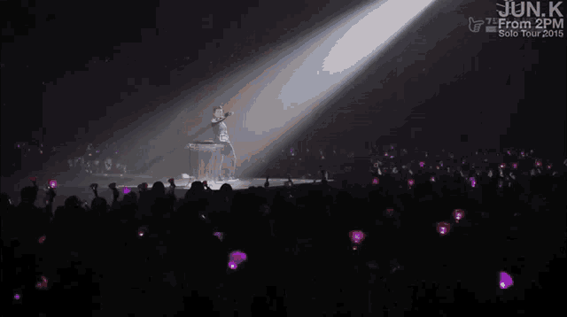 a man stands on a stage in front of a crowd and the words jun.k from 2pm are on the bottom of the screen