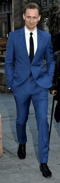 a man in a blue suit and black tie is walking down a sidewalk