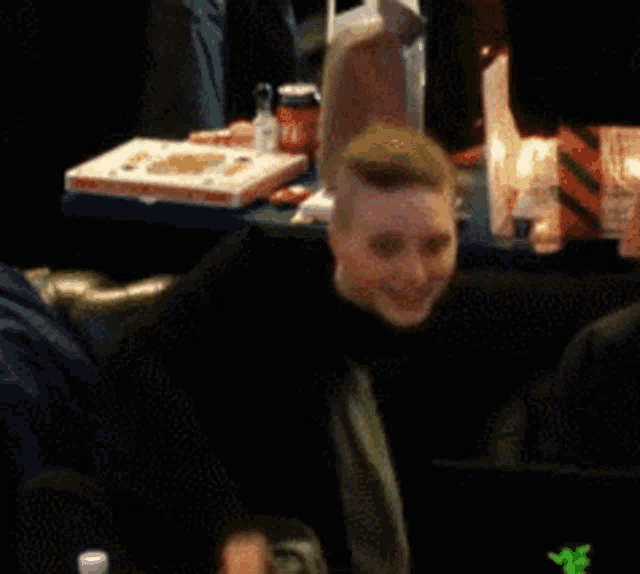 a man sitting at a table with a laptop and a pizza box on it