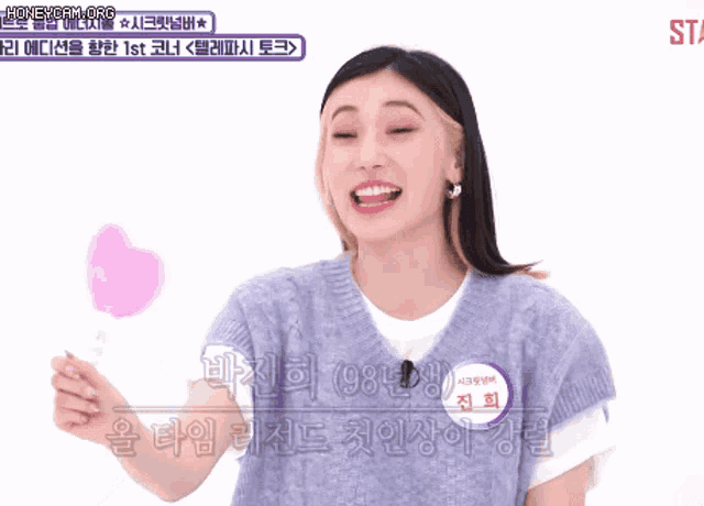 a woman in a sweater vest is holding a pink heart shaped lollipop
