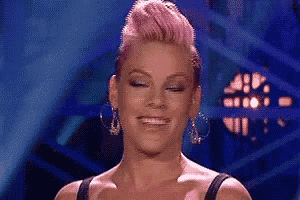 a woman with pink hair and earrings is smiling with her eyes closed .