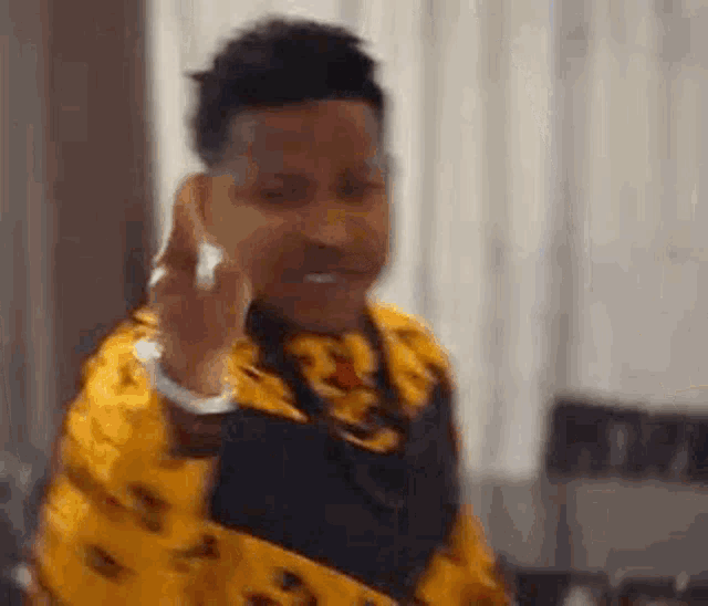 a man in a yellow shirt is making a funny face while talking on a cell phone .