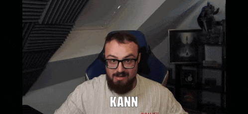 a man with glasses and a beard is wearing a white shirt that says kann