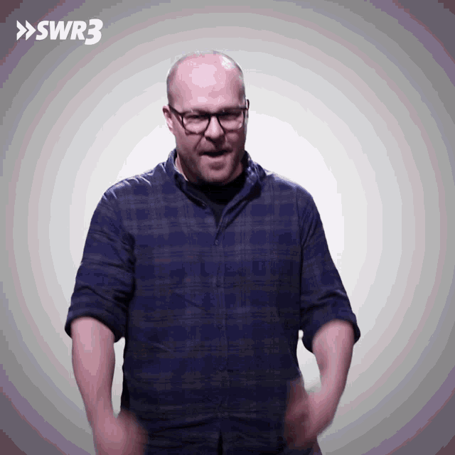 a man wearing glasses and a blue plaid shirt stands in front of a swr3 sign
