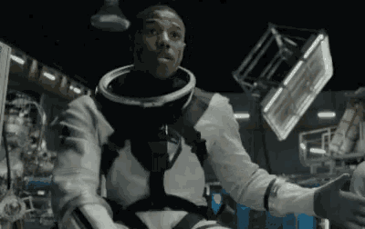 a man in an astronaut 's suit is sitting in a room with his arms outstretched .