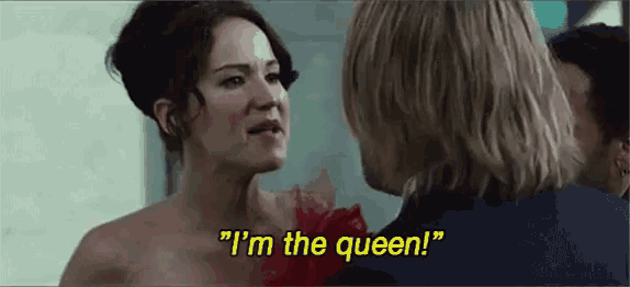 a woman in a dress is talking to a man in a suit and says `` i 'm the queen '' .
