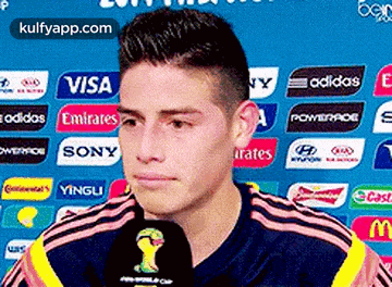 a soccer player is talking into a microphone while standing in front of a sign that says visa emirates .