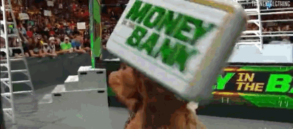 a wrestler is holding a money bank on his head .