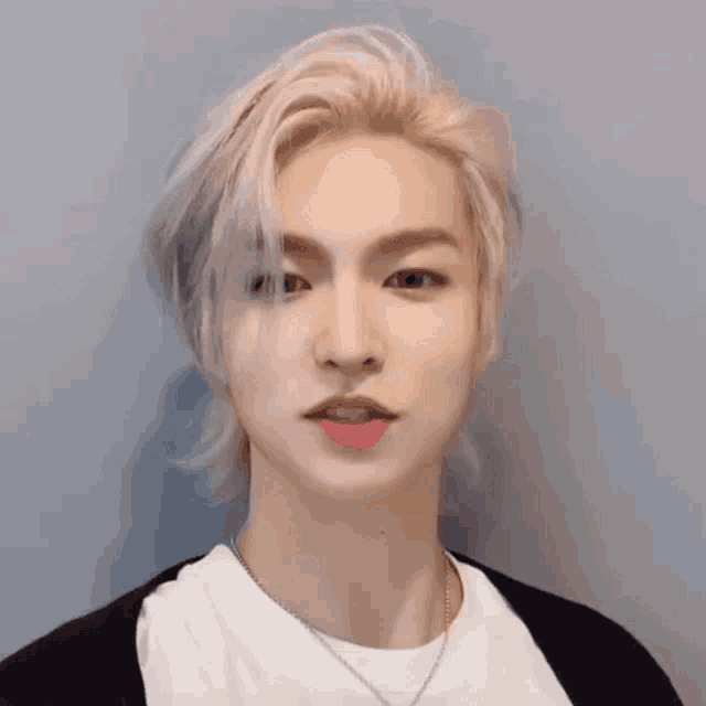a close up of a young man with blonde hair wearing a white shirt and a black cardigan .