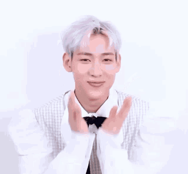 a young man with white hair and a white shirt and tie is clapping his hands .