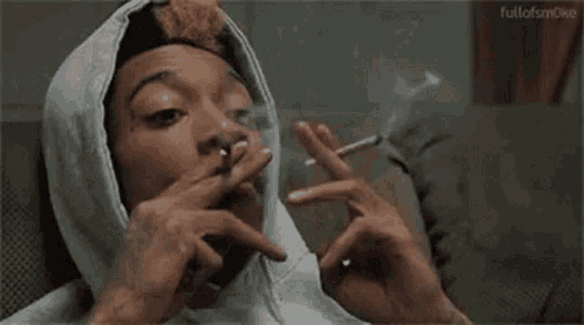 a man in a hooded sweatshirt is smoking a cigarette .