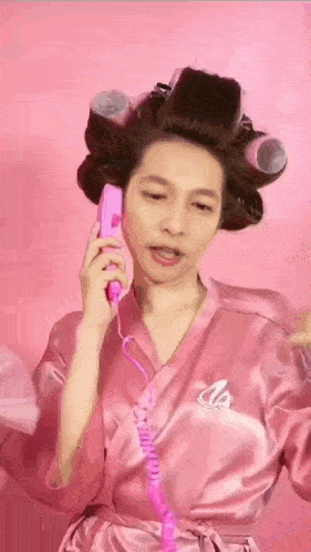 a woman in a pink robe with curlers in her hair is talking on a pink telephone .