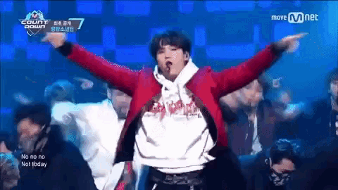 a man in a red jacket is dancing on a stage with his arms outstretched in front of a crowd .