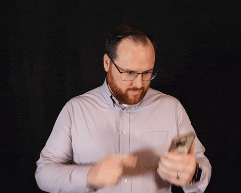 a man with glasses and a beard is looking at his cell phone