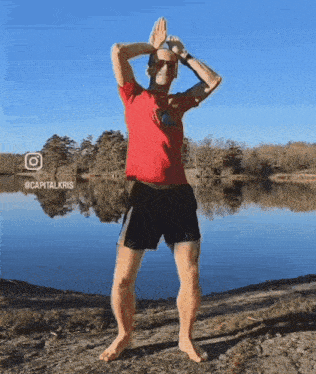 a man in a red shirt and black shorts is standing in front of a body of water ..