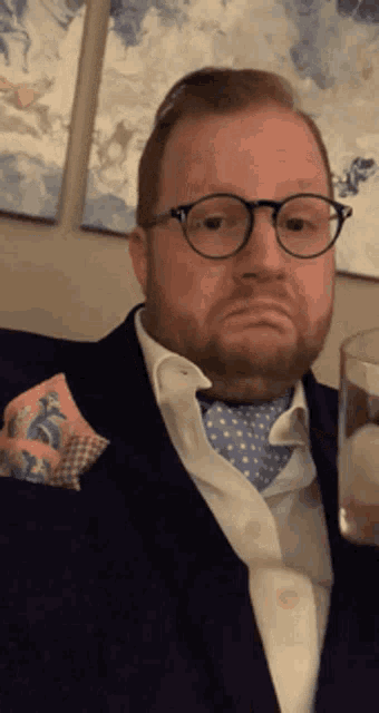a man wearing glasses and a tie is holding a glass