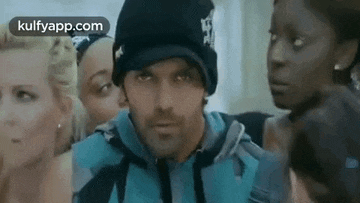 a man wearing a hat and a hoodie is standing in front of a group of women .