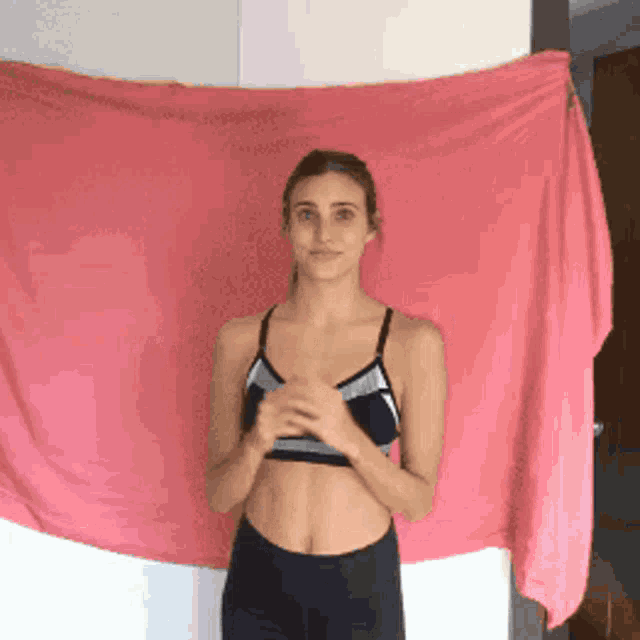a woman in a sports bra stands in front of a large pink towel