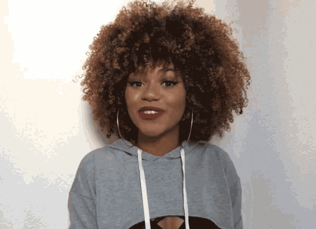 a woman with curly hair wearing a gray hoodie