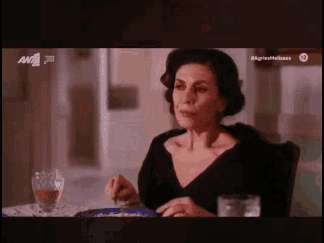 a woman sits at a table with a plate of food and a glass of wine in front of a screen that says agriesmelisses