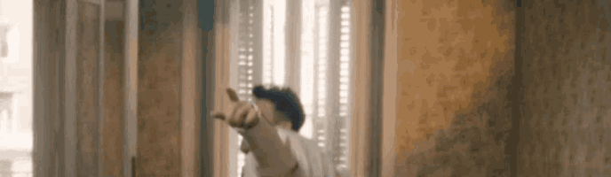 a man is pointing at the camera while standing in front of a window in a room .