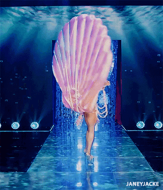 a woman in a seashell costume is walking down a runway with the words janeyjacke below her