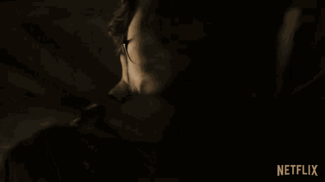 a man wearing glasses covering his face with a scarf with a netflix logo behind him
