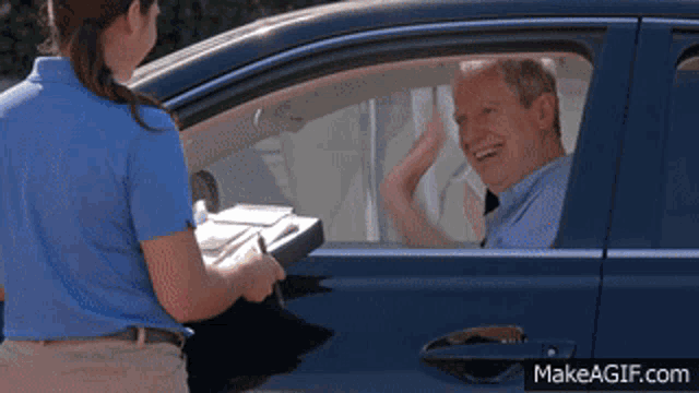 a woman in a blue shirt is serving a man in a blue car